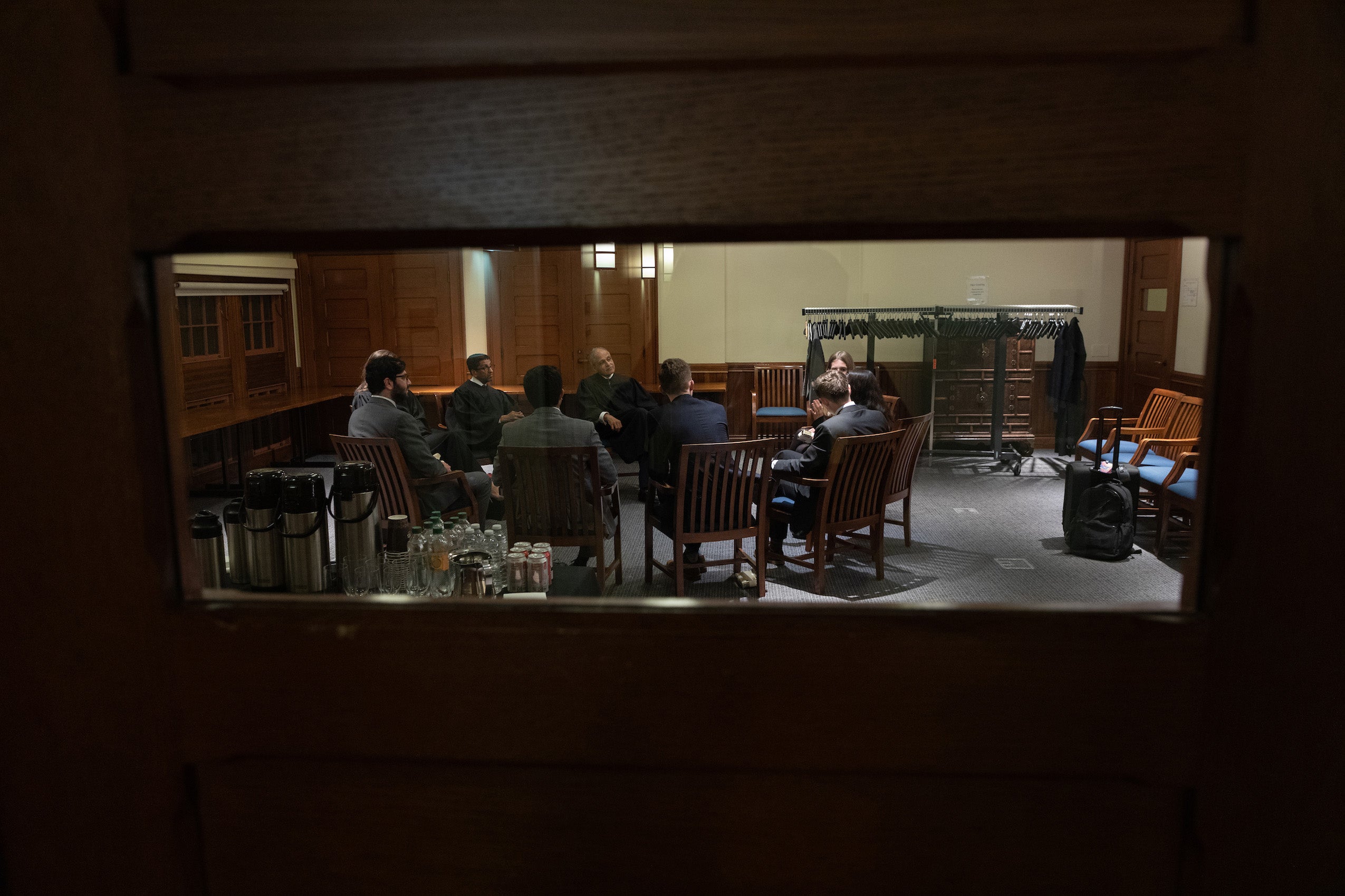 A through the window view of judges and students sitting in a circle speaking to each other